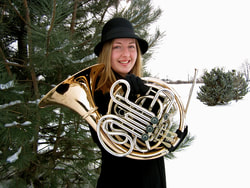 Holding a horn in front of an evergreen tree in the snow